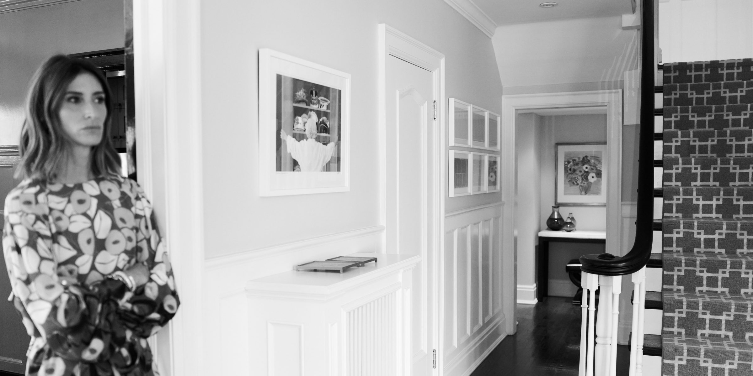 Framed works installed along the hallway and staircase of a Toronto home, with Jo Jo Whitefield standing at left