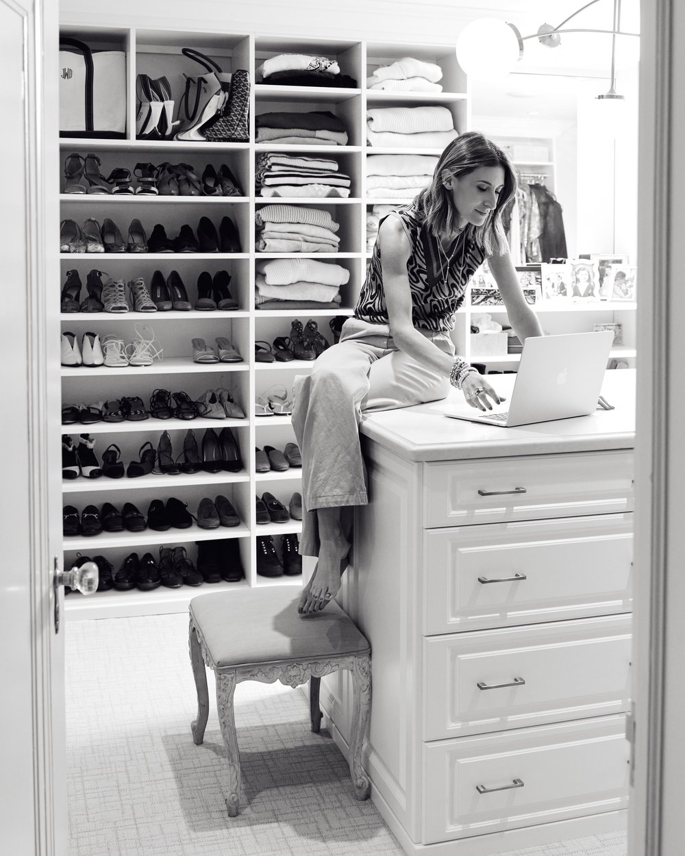 Jo Jo Whitefield working at a laptop in a dressing room lined with shelved shoes and folded knitwear